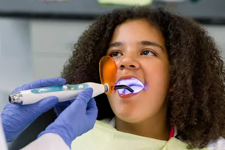 A person seated in a dental chair receiving treatment with a large dental device positioned near their head.