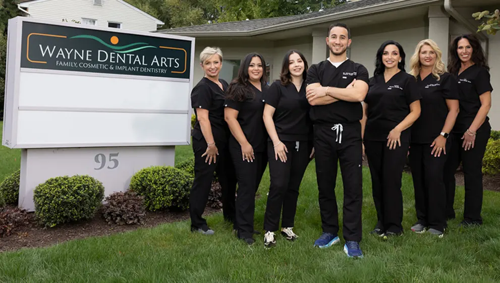 The doctor and staff of Wayne Dental Arts smiling in a group picture in front of their practice sign